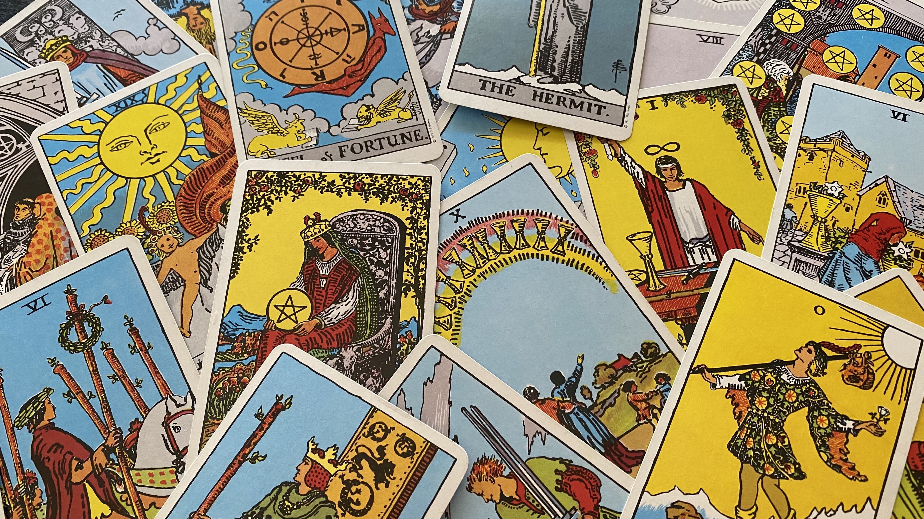 A scattered pile of colorful Rider-Waite tarot cards including The Sun and The Hermit.