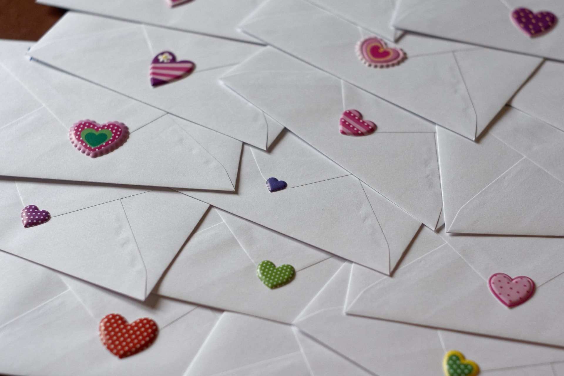 Multiple white envelopes scattered together, each sealed with a different colorful, patterned heart sticker.